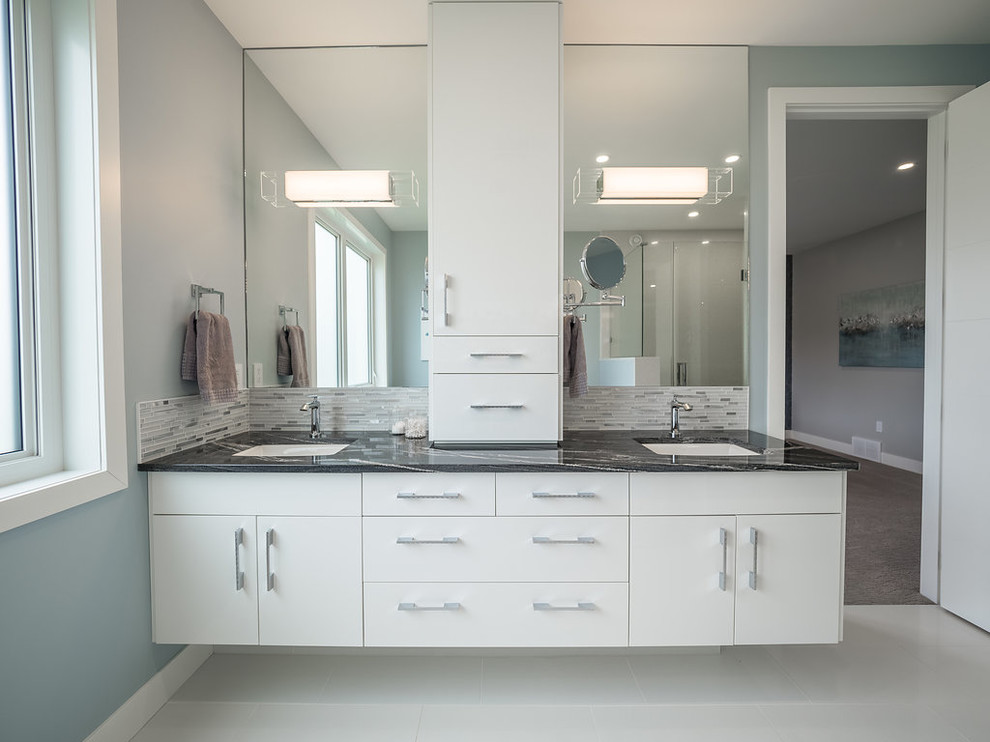 Inspiration for a large contemporary master bathroom in Edmonton with flat-panel cabinets, white cabinets, a drop-in tub, a double shower, a two-piece toilet, white tile, glass tile, blue walls, porcelain floors, a drop-in sink, granite benchtops, white floor and a hinged shower door.