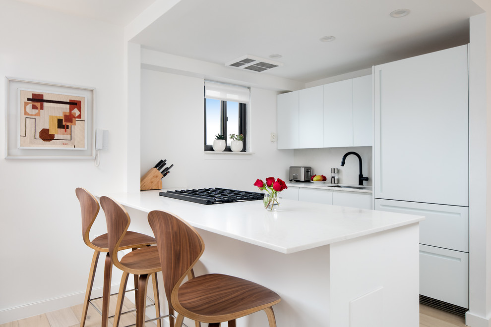 Inspiration for a contemporary galley kitchen in Charleston with an undermount sink, flat-panel cabinets, white cabinets, white splashback, white appliances, light hardwood floors, a peninsula, beige floor and white benchtop.