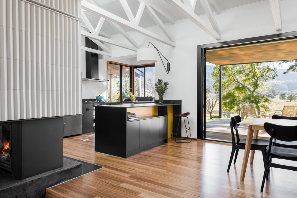 Large midcentury eat-in kitchen in Other with medium hardwood floors, flat-panel cabinets, black cabinets, white splashback, a peninsula, brown floor and black benchtop.