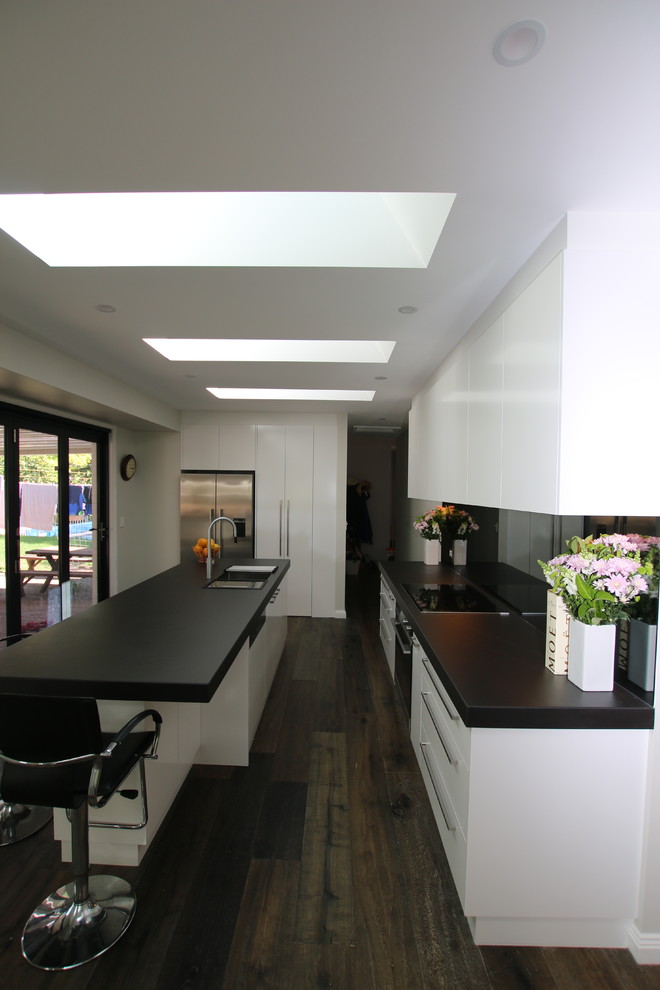 Inspiration for a large l-shaped kitchen pantry in Sydney with an undermount sink, flat-panel cabinets, white cabinets, tile benchtops, black splashback, mirror splashback, stainless steel appliances, medium hardwood floors and with island.