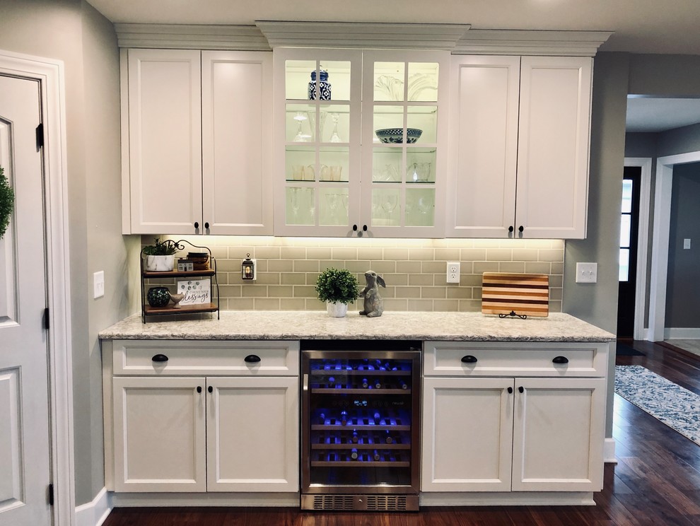 This is an example of an expansive country eat-in kitchen in New York with an undermount sink, shaker cabinets, white cabinets, quartz benchtops, white splashback, ceramic splashback, stainless steel appliances, medium hardwood floors, with island, multi-coloured floor and white benchtop.