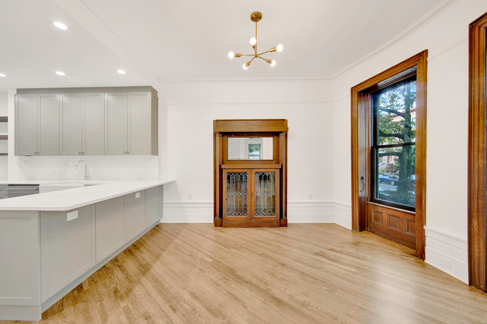 Large transitional kitchen/dining combo in New York with white walls, light hardwood floors, a standard fireplace, a wood fireplace surround and beige floor.