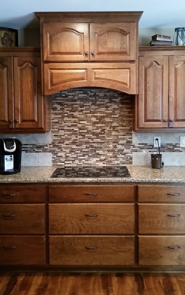 Example of a mid-sized mountain style medium tone wood floor kitchen design with raised-panel cabinets, medium tone wood cabinets, quartz countertops, multicolored backsplash and mosaic tile backsplash