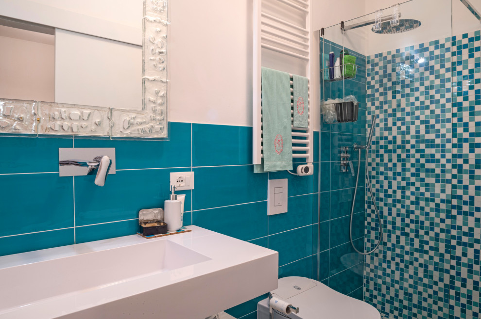 Photo of a small contemporary cloakroom in Florence with a one-piece toilet, green tiles, ceramic tiles, light hardwood flooring, a wall-mounted sink, solid surface worktops and white worktops.