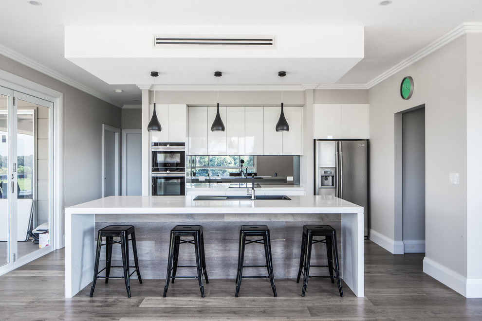 Large modern galley kitchen pantry in Sydney with a drop-in sink, flat-panel cabinets, white cabinets, quartz benchtops, black splashback, glass sheet splashback, stainless steel appliances, plywood floors, with island and grey floor.