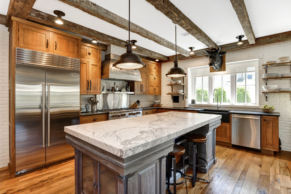 Photo of a country l-shaped kitchen in New York with a farmhouse sink, shaker cabinets, medium wood cabinets, white splashback, brick splashback, stainless steel appliances, medium hardwood floors, with island, brown floor and white benchtop.
