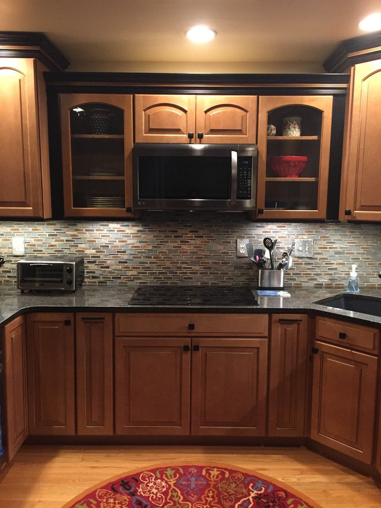 This is an example of a small country u-shaped kitchen in Other with a single-bowl sink, raised-panel cabinets, brown cabinets, quartz benchtops, mosaic tile splashback and light hardwood floors.