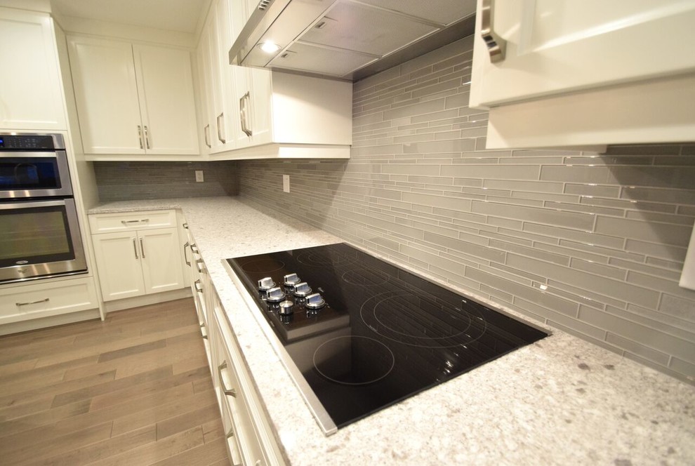 Eat-in kitchen - transitional l-shaped vinyl floor eat-in kitchen idea in Edmonton with a double-bowl sink, shaker cabinets, white cabinets, quartz countertops, gray backsplash, glass tile backsplash, stainless steel appliances and an island