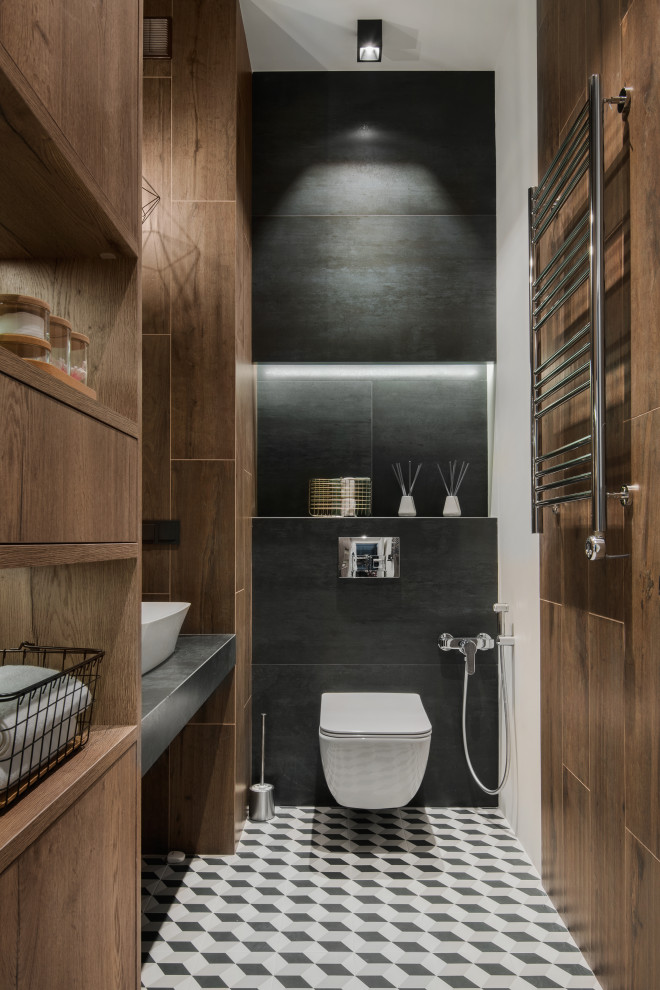 Inspiration for a small laundry room in Moscow with a drop-in sink, flat-panel cabinets, medium wood cabinets, tile benchtops, brown walls, ceramic floors, a stacked washer and dryer, grey floor and black benchtop.