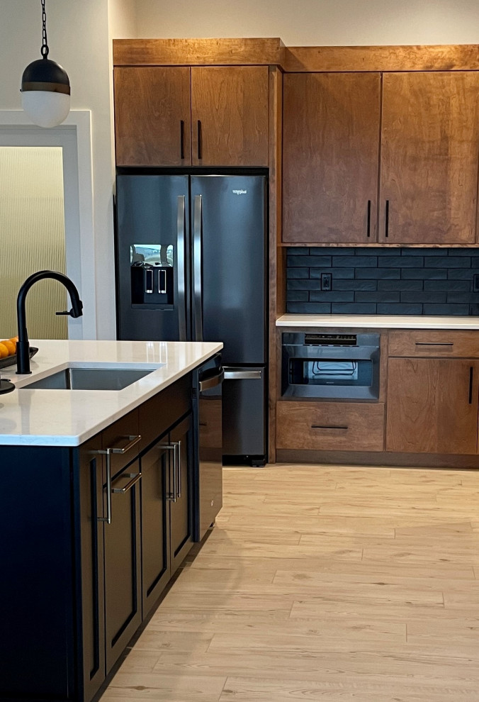 Photo of a large retro l-shaped open plan kitchen in Other with a submerged sink, flat-panel cabinets, medium wood cabinets, engineered stone countertops, black splashback, metro tiled splashback, black appliances, light hardwood flooring, an island, brown floors and white worktops.