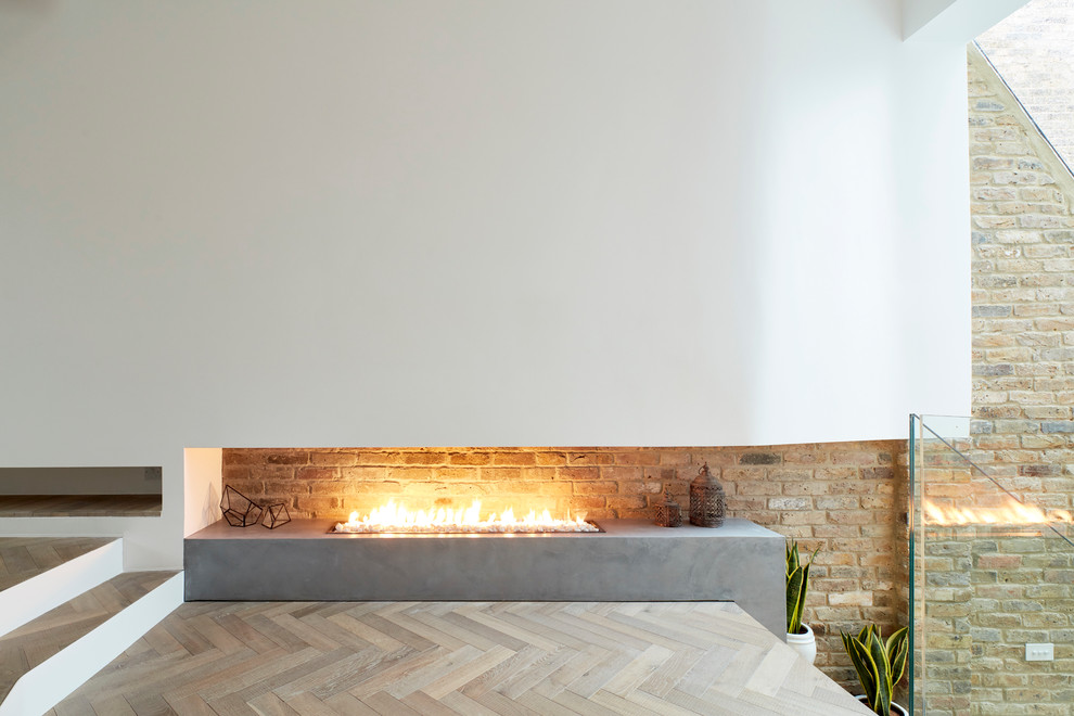 Photo of a large contemporary open concept living room in London with a library, white walls, medium hardwood floors, a ribbon fireplace, a concrete fireplace surround and a wall-mounted tv.