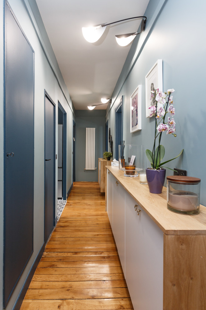 This is an example of a contemporary hallway in Paris with blue walls, medium hardwood floors and beige floor.