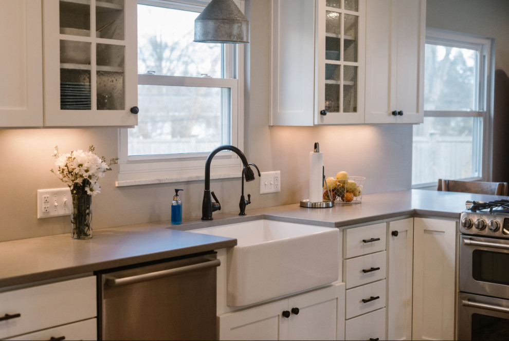 Mid-sized transitional l-shaped medium tone wood floor and brown floor eat-in kitchen photo in Columbus with a farmhouse sink, shaker cabinets, white cabinets, solid surface countertops, gray backsplash, matchstick tile backsplash, stainless steel appliances and no island
