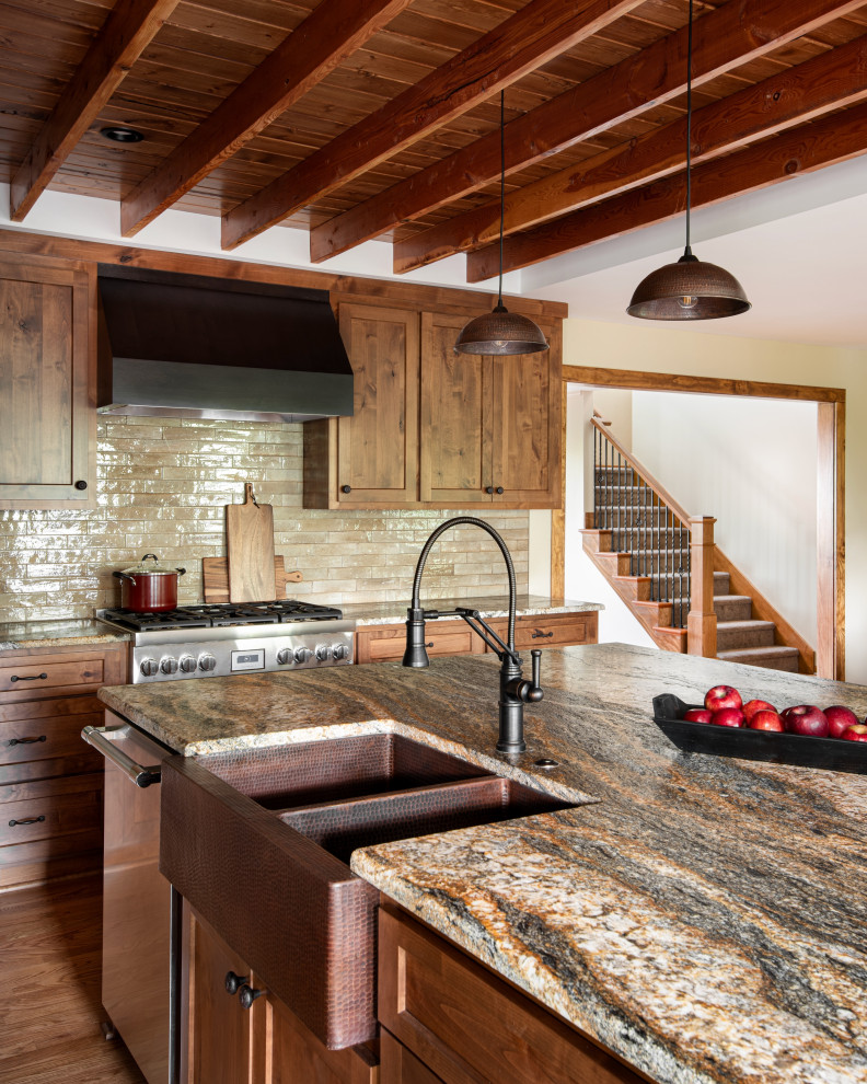 Large country l-shaped eat-in kitchen in Kansas City with a farmhouse sink, shaker cabinets, medium wood cabinets, granite benchtops, beige splashback, ceramic splashback, stainless steel appliances, medium hardwood floors, with island, brown floor, multi-coloured benchtop and exposed beam.