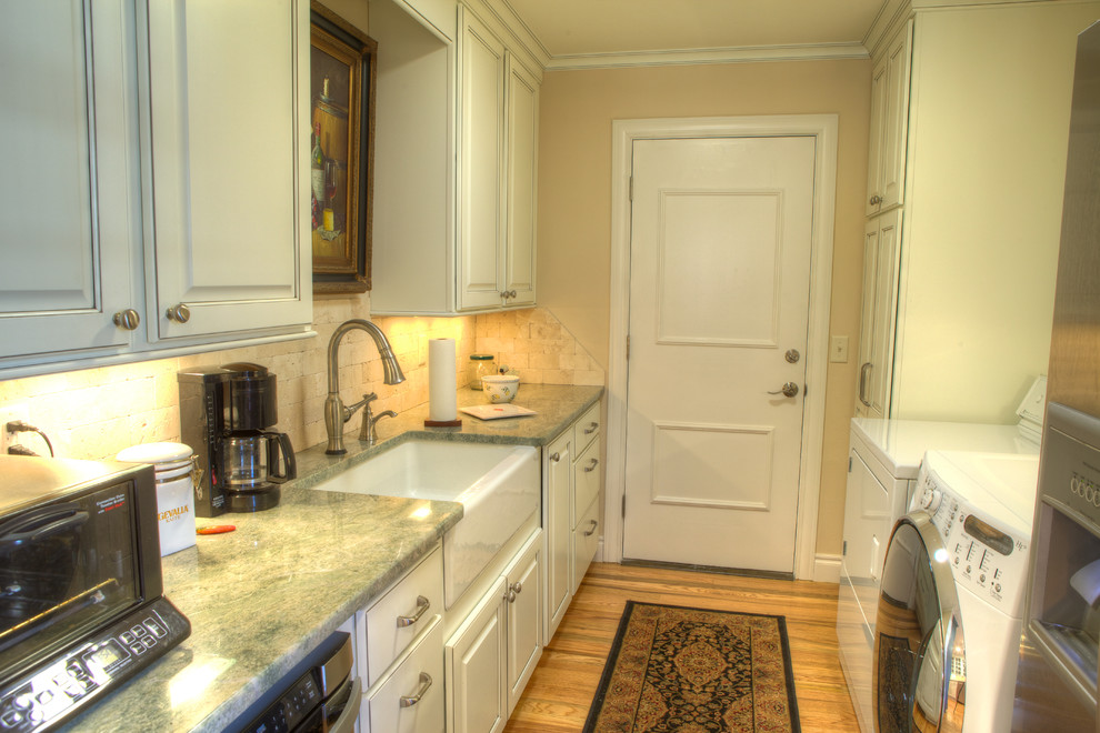 Design ideas for a mid-sized traditional galley utility room in Oklahoma City with a farmhouse sink, raised-panel cabinets, white cabinets, granite benchtops, beige walls, light hardwood floors, a side-by-side washer and dryer and beige floor.