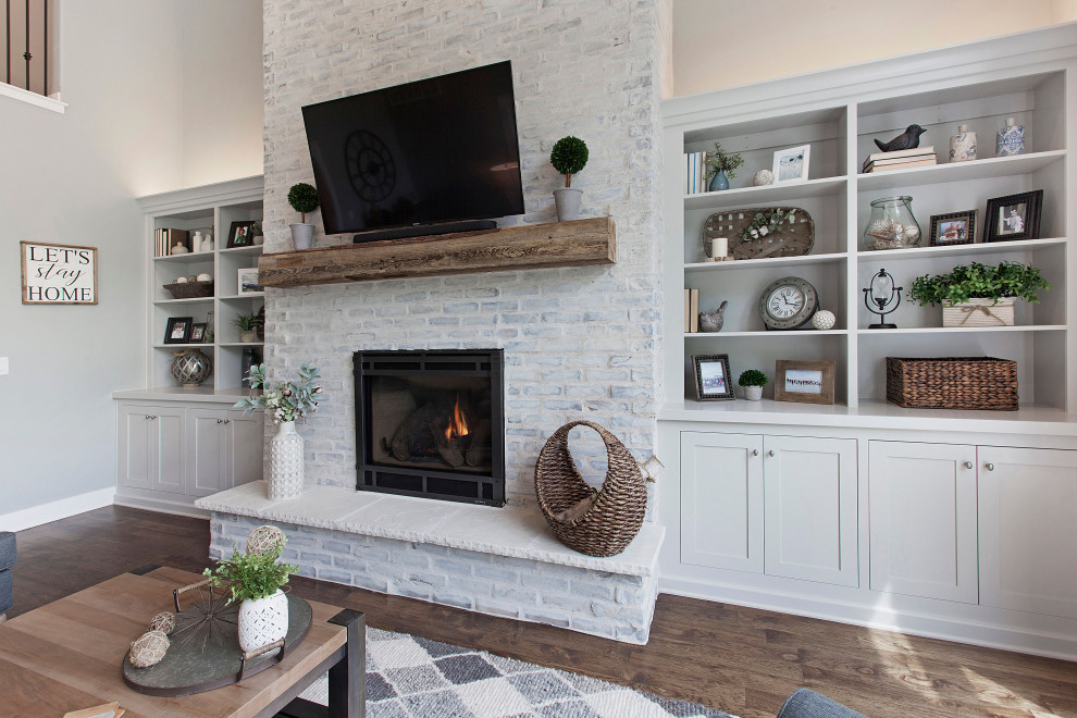 Photo of a mid-sized country loft-style living room in Kansas City with grey walls, a standard fireplace, a wall-mounted tv, medium hardwood floors, a brick fireplace surround and brown floor.