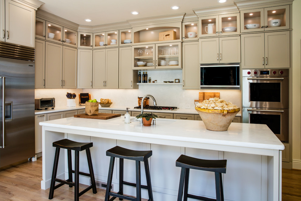 Inspiration for a mid-sized traditional l-shaped eat-in kitchen in San Francisco with a single-bowl sink, recessed-panel cabinets, beige cabinets, marble benchtops, beige splashback, porcelain splashback, stainless steel appliances, light hardwood floors, with island and beige floor.