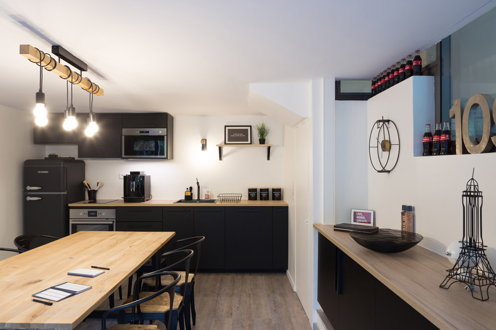 Photo of a mid-sized industrial l-shaped separate kitchen in Paris with a single-bowl sink, beaded inset cabinets, black cabinets, wood benchtops, white splashback, stainless steel appliances, linoleum floors, no island, grey floor and brown benchtop.