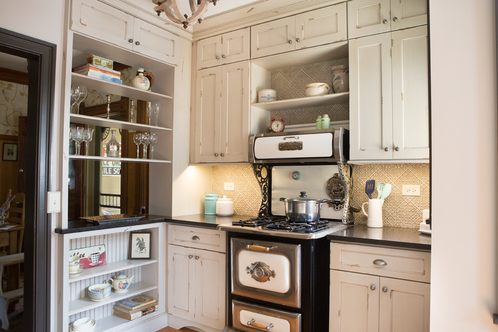 This is an example of a small traditional galley kitchen pantry in Chicago with a farmhouse sink, beige cabinets, granite benchtops, beige splashback, ceramic splashback, panelled appliances, medium hardwood floors, no island, brown floor, black benchtop and flat-panel cabinets.
