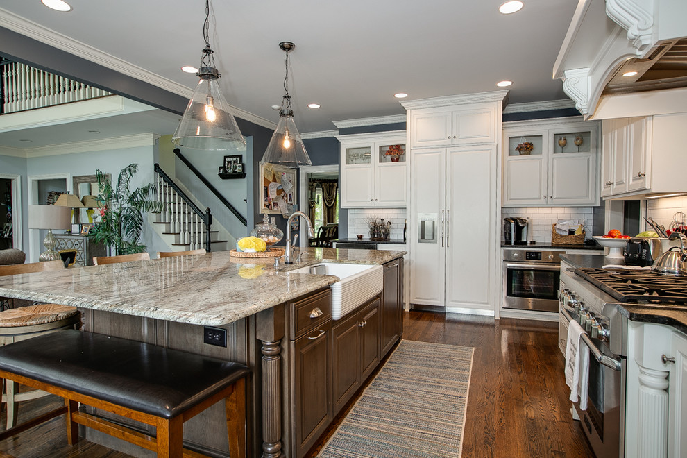 Inspiration for a large transitional l-shaped medium tone wood floor and brown floor open concept kitchen remodel in Charlotte with a farmhouse sink, white cabinets, granite countertops, white backsplash, stainless steel appliances, an island, raised-panel cabinets, porcelain backsplash and white countertops