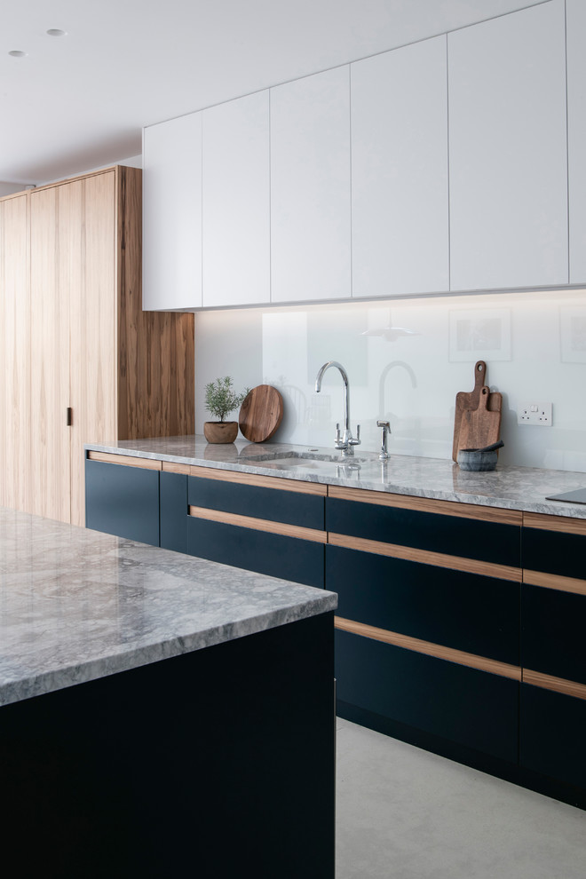 Inspiration for a mid-sized contemporary single-wall open plan kitchen in London with a drop-in sink, flat-panel cabinets, blue cabinets, quartzite benchtops, glass sheet splashback, black appliances, ceramic floors, with island and grey benchtop.