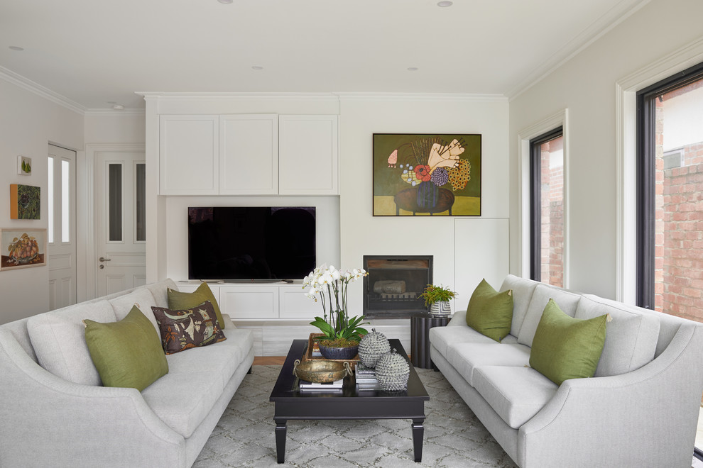 Photo of a transitional family room in Melbourne with white walls, medium hardwood floors, a standard fireplace, a freestanding tv and brown floor.