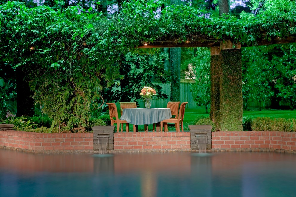 Photo of a mid-sized traditional backyard custom-shaped natural pool in Houston with a water feature and brick pavers.