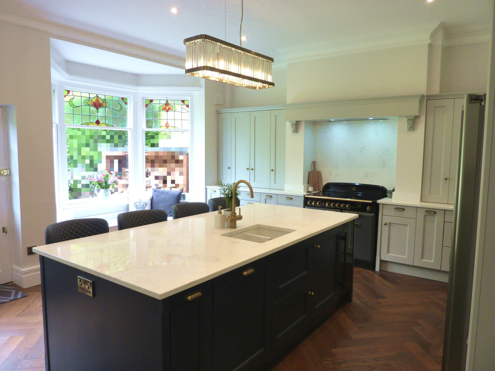 Large classic grey and teal u-shaped enclosed kitchen in West Midlands with a belfast sink, beaded cabinets, grey cabinets, quartz worktops, white splashback, marble splashback, coloured appliances, medium hardwood flooring, an island, white worktops and a chimney breast.