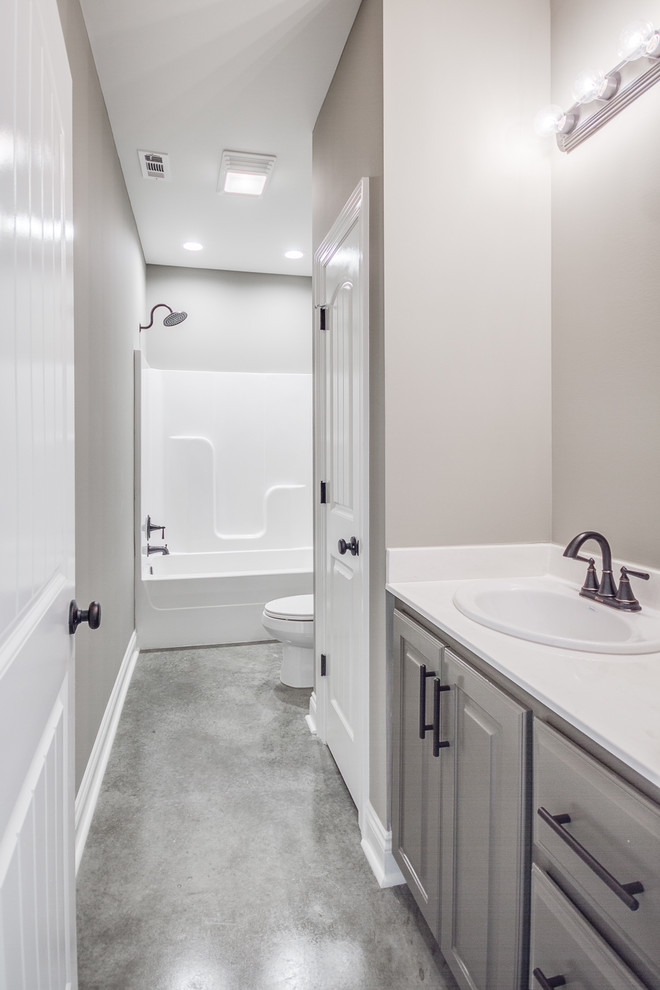 This is an example of a mid-sized transitional 3/4 bathroom in New Orleans with raised-panel cabinets, grey cabinets, a shower/bathtub combo, a two-piece toilet, grey walls, concrete floors, a drop-in sink, marble benchtops, grey floor and white benchtops.