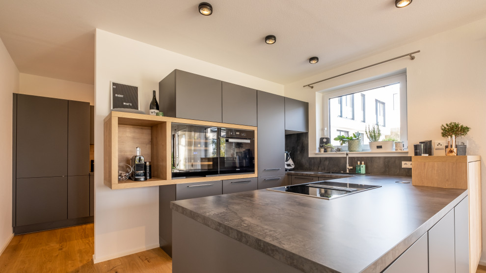 Mid-sized contemporary u-shaped eat-in kitchen in Other with flat-panel cabinets, grey cabinets, black appliances, a peninsula, brown floor and grey benchtop.