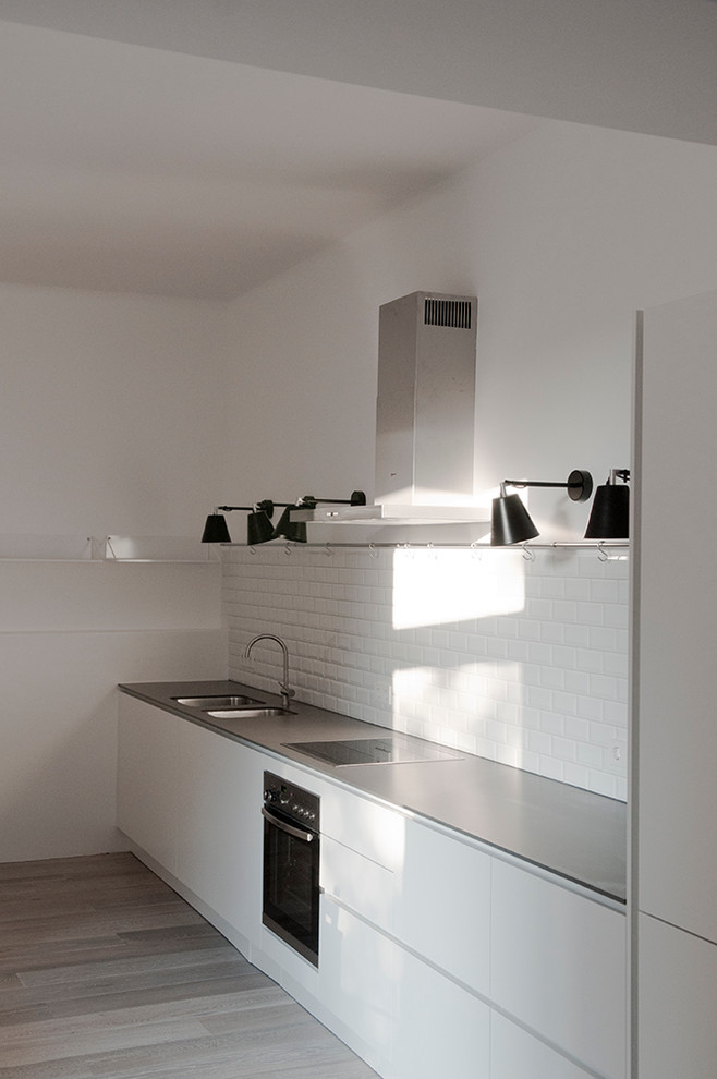 Mid-sized contemporary single-wall open plan kitchen in Berlin with a drop-in sink, flat-panel cabinets, white cabinets, quartzite benchtops, white splashback, subway tile splashback, stainless steel appliances and no island.