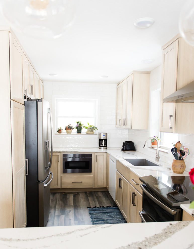 Example of a mid-sized transitional u-shaped vinyl floor and brown floor enclosed kitchen design with an undermount sink, flat-panel cabinets, beige cabinets, quartz countertops, white backsplash, subway tile backsplash, black appliances, a peninsula and white countertops