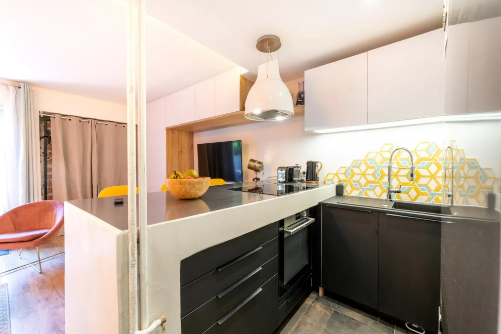 Aménagement de cuisine américaine in L With un évier 1 bac, un placard à porte affleurante, des portes de placard blanches, un plan de travail en inox, une crédence multicolore, une crédence en carreau de ciment, un électroménager noir, parquet clair, îlot, un sol beige, plan de travail noir and un plafond décaissé.