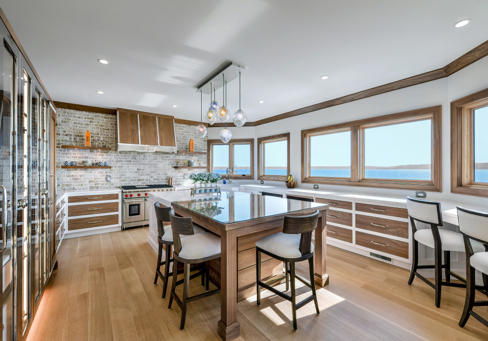 Mid-sized transitional u-shaped kitchen in New York with flat-panel cabinets, medium wood cabinets, light hardwood floors, with island and white benchtop.