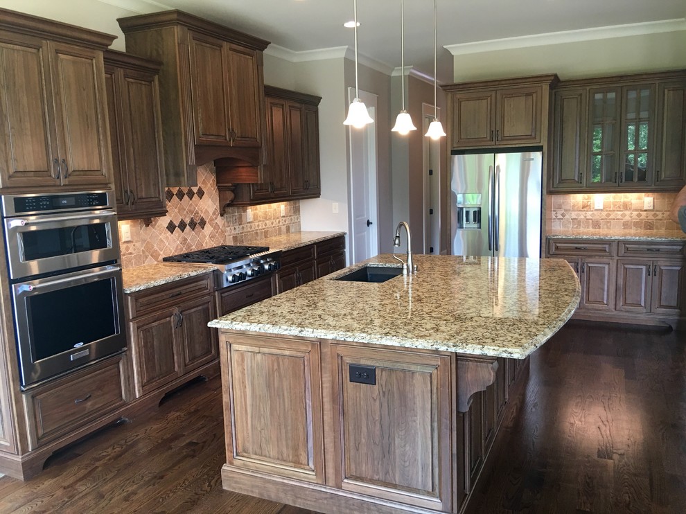 This is an example of a large transitional l-shaped kitchen in Atlanta with an undermount sink, raised-panel cabinets, medium wood cabinets, granite benchtops, beige splashback, mosaic tile splashback, stainless steel appliances, dark hardwood floors and with island.