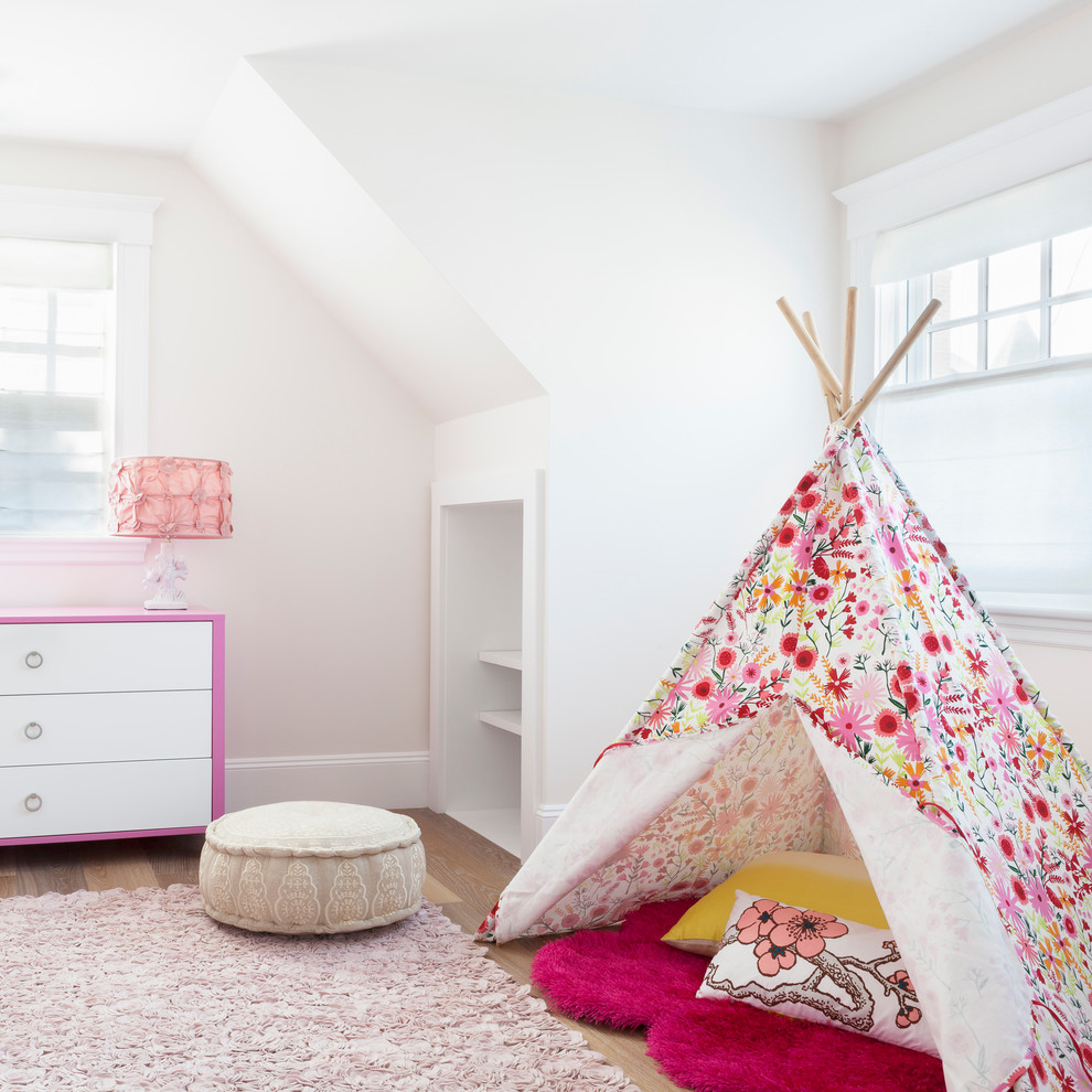 This is an example of a beach style kids' bedroom for kids 4-10 years old and girls in New York with white walls, medium hardwood floors and beige floor.