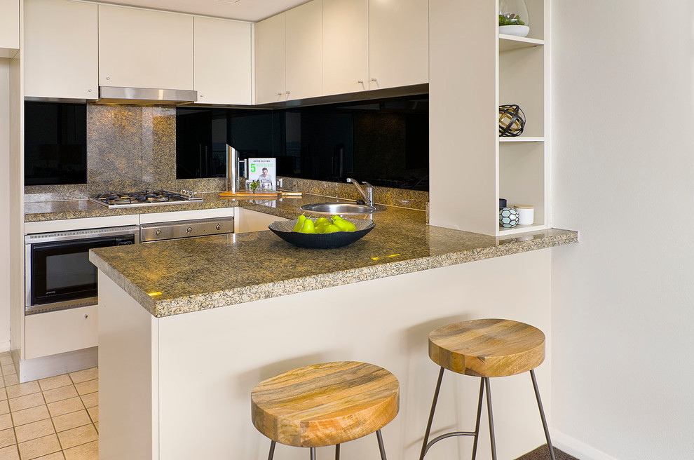 Design ideas for a small contemporary u-shaped open plan kitchen in Sydney with a single-bowl sink, flat-panel cabinets, beige cabinets, granite benchtops, black splashback, glass sheet splashback, stainless steel appliances, porcelain floors, a peninsula, beige floor and beige benchtop.