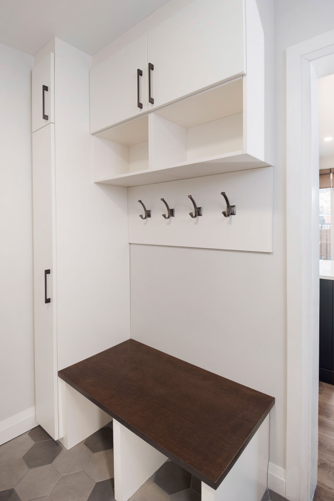 Small modern galley utility room in Ottawa with a single-bowl sink, flat-panel cabinets, white cabinets, quartz worktops, white splashback, ceramic splashback, white walls, ceramic flooring, a stacked washer and dryer, black worktops and multi-coloured floors.