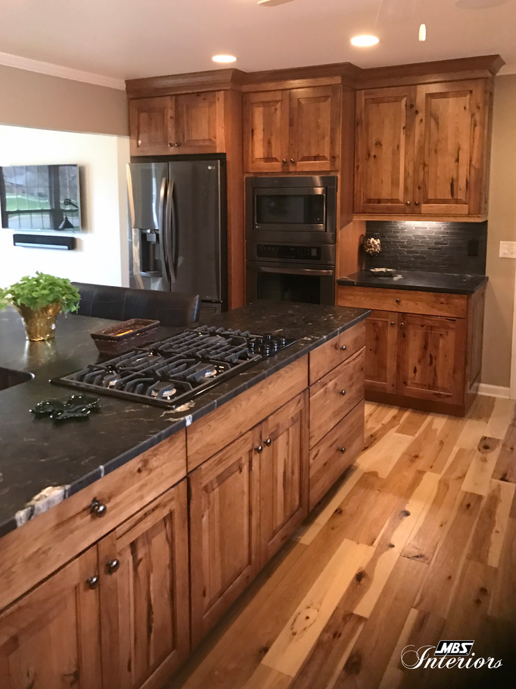 Large mountain style l-shaped light wood floor and beige floor eat-in kitchen photo with an undermount sink, raised-panel cabinets, medium tone wood cabinets, granite countertops, gray backsplash, ceramic backsplash, stainless steel appliances and an island