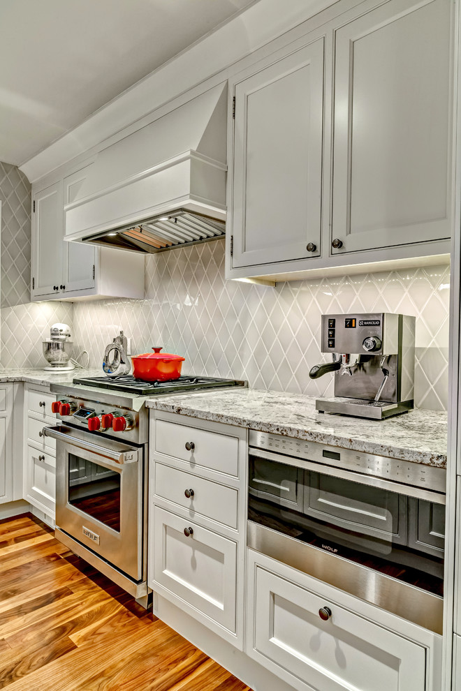 Example of a mid-sized transitional single-wall medium tone wood floor open concept kitchen design in Calgary with an undermount sink, white cabinets, shaker cabinets, granite countertops, gray backsplash, glass tile backsplash, stainless steel appliances and an island