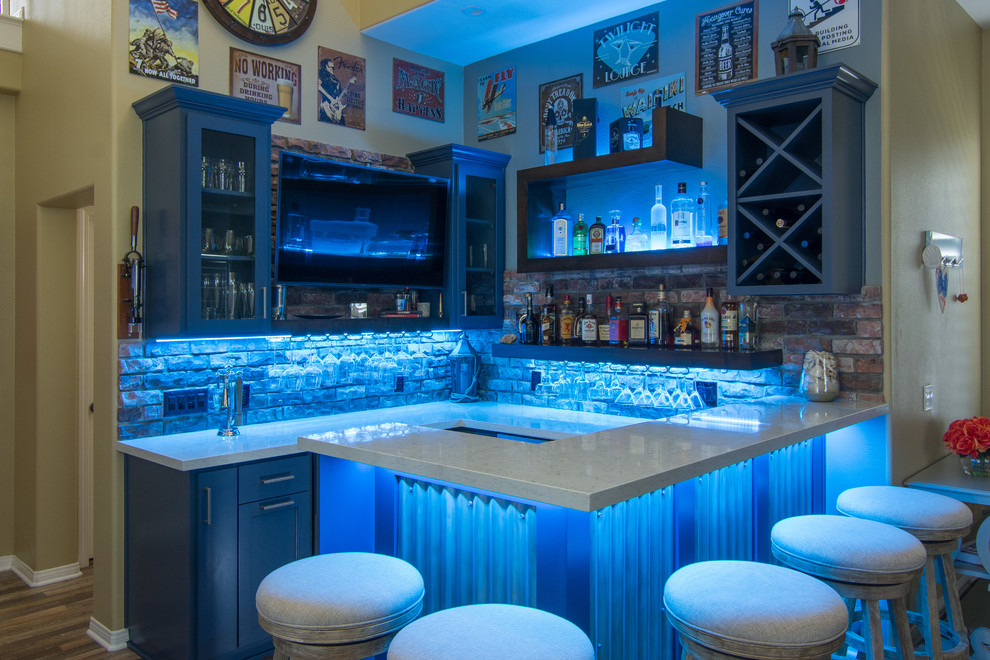 This is an example of a small country u-shaped seated home bar in Los Angeles with no sink, shaker cabinets, blue cabinets, quartz benchtops, multi-coloured splashback, terra-cotta splashback, porcelain floors and brown floor.