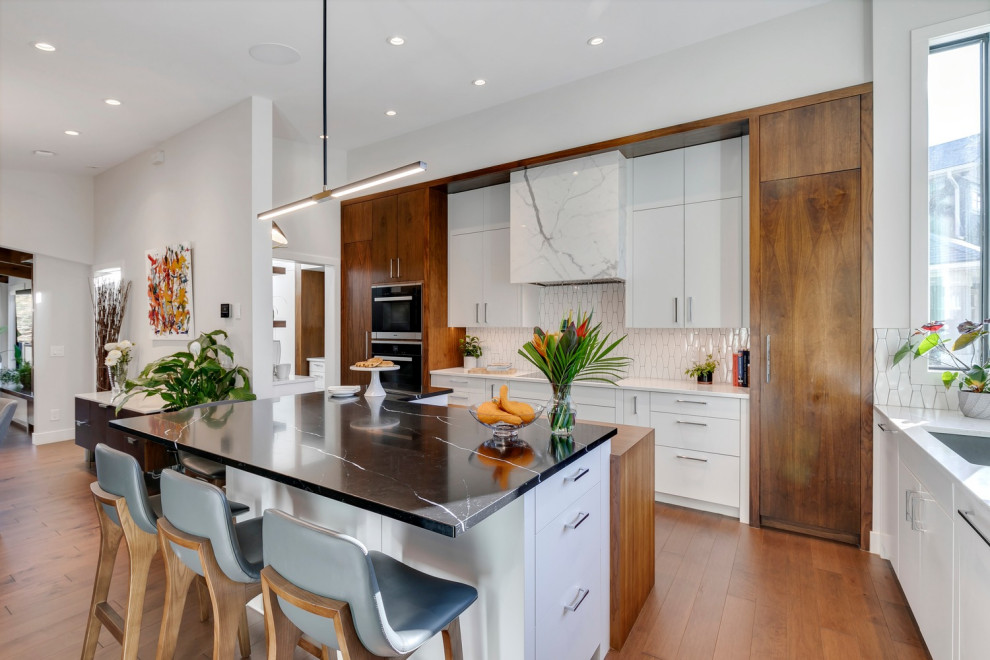 Inspiration for a midcentury kitchen with an undermount sink, flat-panel cabinets, medium wood cabinets, white splashback, ceramic splashback, stainless steel appliances, with island and brown floor.