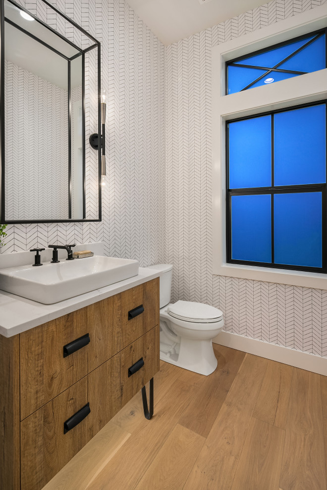 Photo of a mid-sized country powder room in Seattle with furniture-like cabinets, medium wood cabinets, a two-piece toilet, white tile, medium hardwood floors, a vessel sink, beige floor and white benchtops.