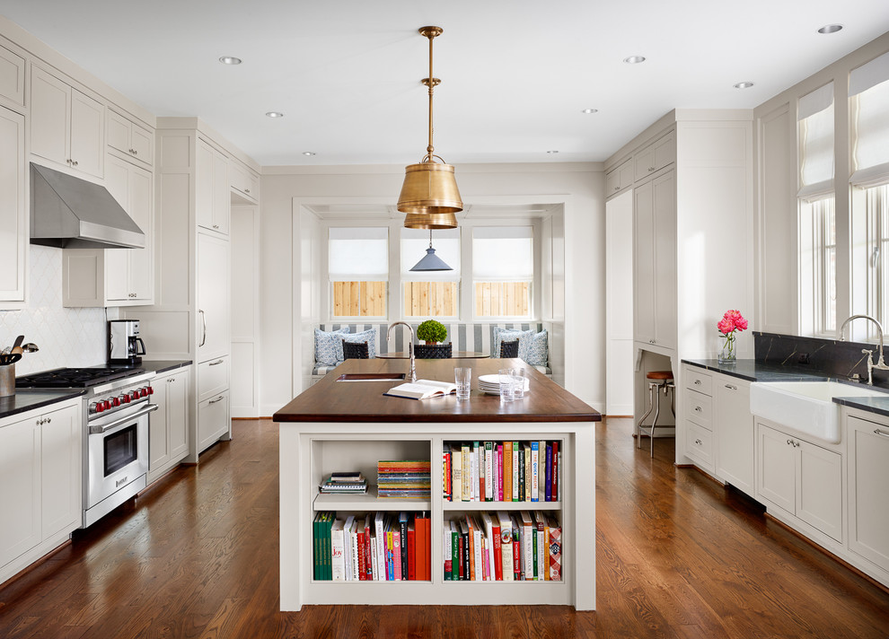 Design ideas for a traditional eat-in kitchen in Houston with a farmhouse sink, shaker cabinets, white splashback, ceramic splashback, panelled appliances, medium hardwood floors and with island.
