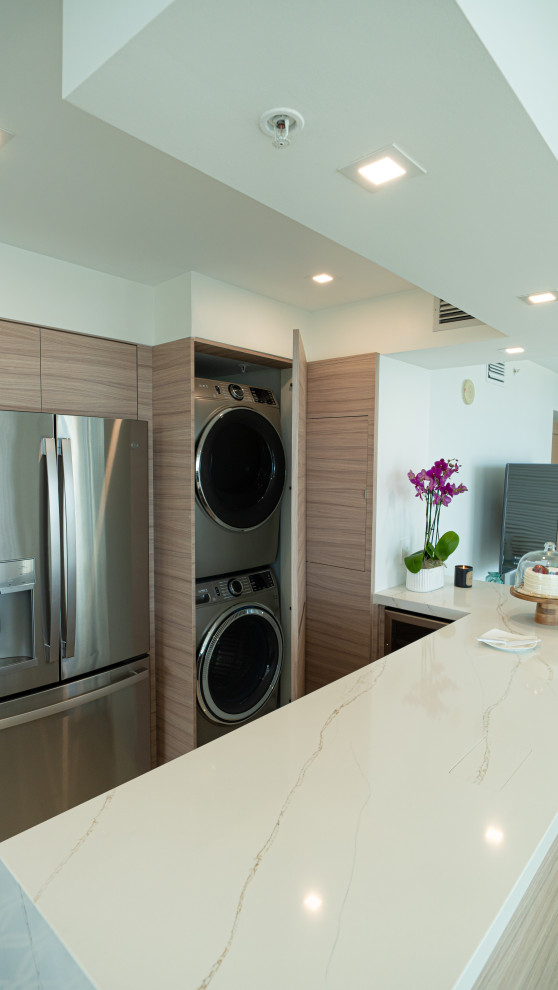 This is an example of a small modern laundry cupboard in Miami with flat-panel cabinets, light wood cabinets, quartz benchtops, marble floors, a stacked washer and dryer, beige floor and beige benchtop.