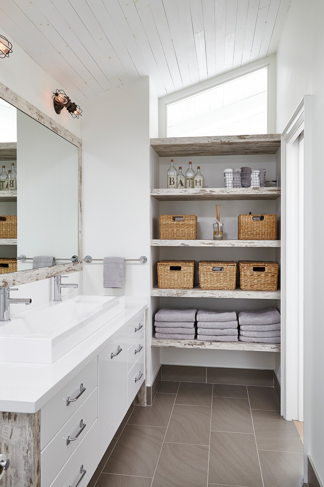 Inspiration for a mid-sized transitional 3/4 bathroom in Toronto with flat-panel cabinets, a two-piece toilet, white walls, porcelain floors, a trough sink, white cabinets, beige tile, solid surface benchtops and white benchtops.
