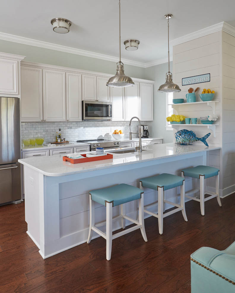 Photo of a beach style single-wall open plan kitchen in Atlanta with an undermount sink, raised-panel cabinets, white cabinets, quartzite benchtops, white splashback, subway tile splashback, stainless steel appliances, dark hardwood floors, with island and brown floor.