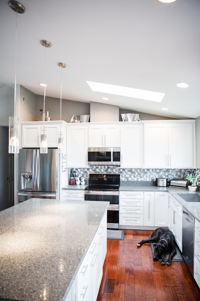 Inspiration for a large transitional l-shaped medium tone wood floor open concept kitchen remodel in Seattle with an undermount sink, flat-panel cabinets, white cabinets, quartz countertops, metallic backsplash, glass tile backsplash, stainless steel appliances and an island