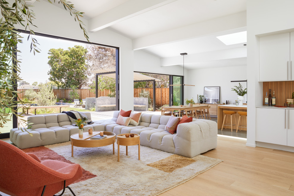 Photo of a large modern open concept living room in San Francisco with a home bar, white walls, light hardwood floors, no fireplace, a wall-mounted tv, brown floor and exposed beam.