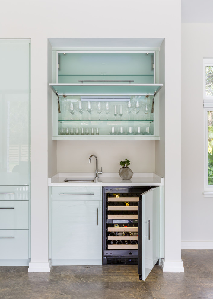 Inspiration for a large contemporary l-shaped home bar in Jacksonville with an undermount sink, flat-panel cabinets, green cabinets, solid surface benchtops, white splashback, concrete floors and brown floor.